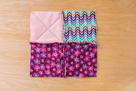 square of sewn fabric made with dark pink floral fabric, light pink fabric, and blue and pink patterned fabric